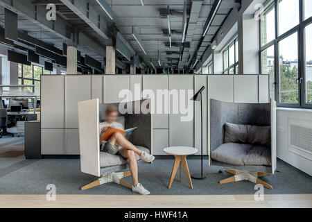 Zona relax nel coworking in stile loft con grandi finestre e pareti di colore grigio. Vi sono di fantasia semi-arrotondato poltrone di colore grigio con cuscini e un piccolo ro Foto Stock