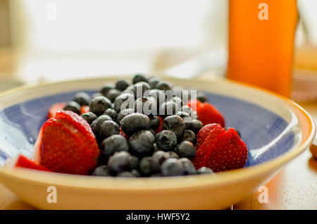 I mirtilli sono lavati e le fragole sono stati tagliati. Si trovano in un vaso blu con uno sfondo luminoso. Foto Stock