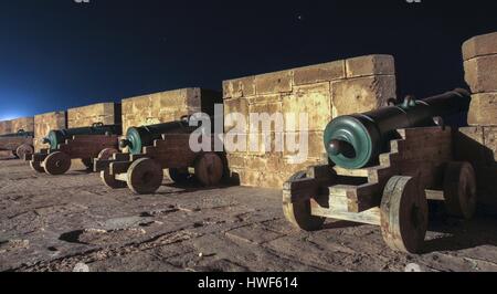 Antica fila di armi canoniche d'epoca illuminata che protegge la famosa Cittadella del forte di pietra mediterranea sotto lo skyline notturno città di Essaouira Marocco Nord Africa Foto Stock