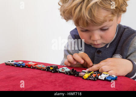 QUEENSTOWN, SUD AFRICA - 17 Maggio 2015 - piccola bionda ragazzo giocando con vintage automobili giocattolo sul velluto rosso pouf sedia - concentrarsi sulle sue mani apertura di un piccolo Foto Stock