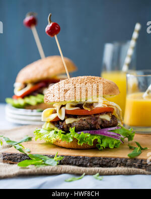 Due hamburger fatti in casa con verdure fresche, carne, cipolle caramellate e formaggio sulla tavola di legno Foto Stock