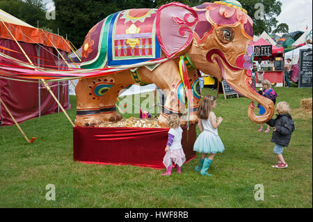 Bambini che giocano davanti a una grande e colorata coperte di seta infantile di elefante di tende e banchi di cibo al porto Eliot Festival Cornovaglia Foto Stock