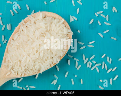 1 cucchiaio di legno essiccato del riso a grani lunghi contro uno sfondo blu Foto Stock