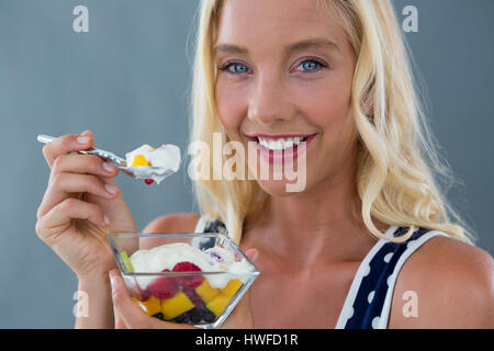 Bella donna di mangiare insalata di frutta in vaso contro uno sfondo grigio Foto Stock