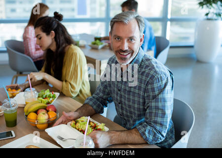 Uomo sorridente con il pasto con i suoi colleghi in ufficio Foto Stock