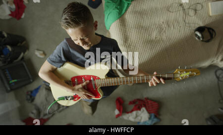 Angolo di alta vista di intensa ragazzo adolescente suonare la chitarra elettrica in camera da letto disordinato Foto Stock