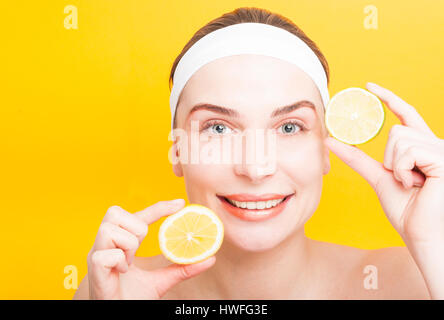 La cura della pelle e concetto di bellezza con gioiosa donna che mostra le fette di limone e lime su sfondo giallo Foto Stock