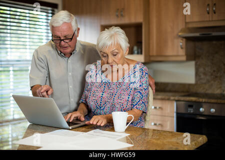 Senior donna utilizzando laptop in cucina a casa Foto Stock