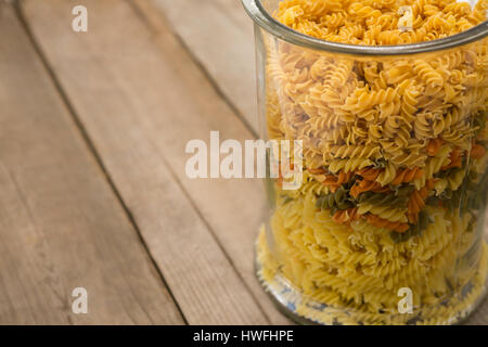 Girandole la pasta in un contenitore di vetro su una superficie di legno Foto Stock