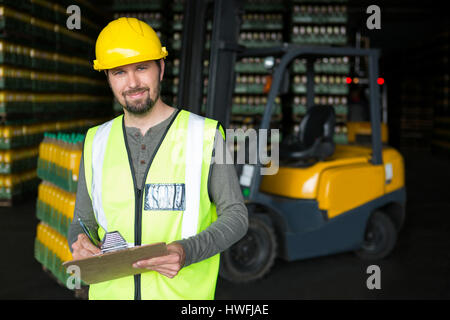 Ritratto di sorridere lavoratore maschile iscritto negli appunti in magazzino Foto Stock