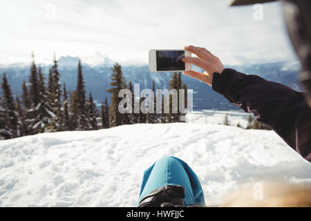 Immagine ritagliata della persona fotografare in coperta di neve montagna contro alberi Foto Stock