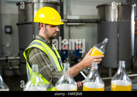 Vista laterale di grave lavoratore di sesso maschile di ispezionare bottiglie in fabbrica di succo Foto Stock