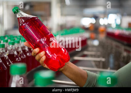 Ritagliate la mano del lavoratore azienda succo rosso Bottiglia in fabbrica Foto Stock