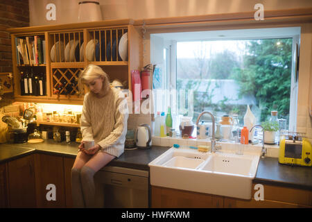 Donna con caffè in cucina a casa Foto Stock