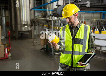 Fiducioso lavoratore di sesso maschile di ispezionare bottiglie in fabbrica di succo Foto Stock