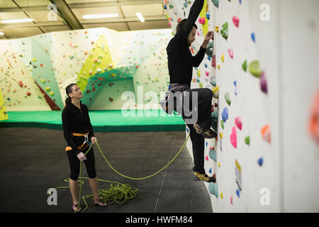 Il Trainer assiste l uomo mentre si arrampica su parete artificiale in palestra Foto Stock