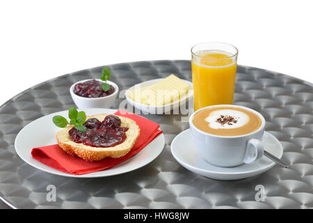 Piccola colazione continentale: un nuovo rotolo di sesamo con marmellata di ciliege, burro, una tazza di cappuccino e un bicchiere di succo d'arancia su un tavolo bistro Foto Stock