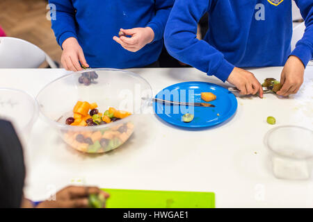 I bambini della scuola elementare di preparare una insalata di frutta in una scuola inglese Foto Stock