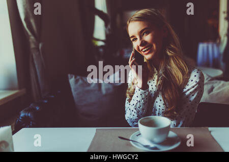 Donna felice di parlare con il telefono cellulare mentre è seduto nella caffetteria durante la colazione del mattino Foto Stock