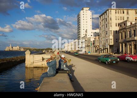 Cuba, La Habana, Malecon, musicisti di strada giocando saxo e trobone davanti la sfilata delle vecchie automobili americane alla fine della giornata Foto Stock