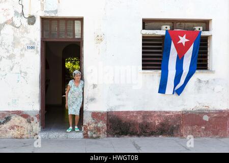 Cuba, Cienfuegos province, Cienfuegos, vecchia donna in piedi dalla porta della sua casa e bandiera cubana Foto Stock