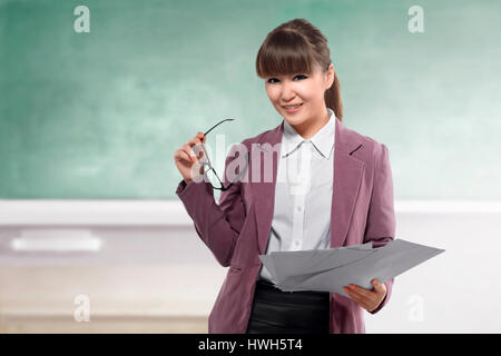 Sorridente insegnante asiatici con carta in piedi di fronte a lavagna di classe Foto Stock