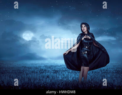 Bella strega donna con mantello cappa camminando sul prato all'aperto Foto Stock