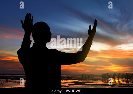 Immagine di silhouette uomo che prega con sfondo al tramonto Foto Stock