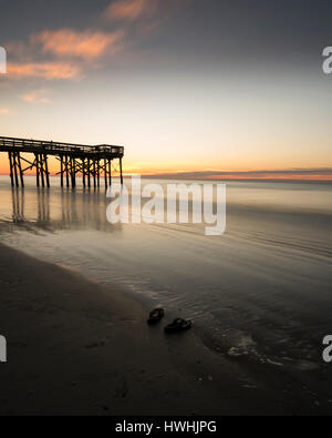 Sunrise con sandali di vuoto sulla spiaggia con pier in background, oceano morbido e caldo nuvole Foto Stock