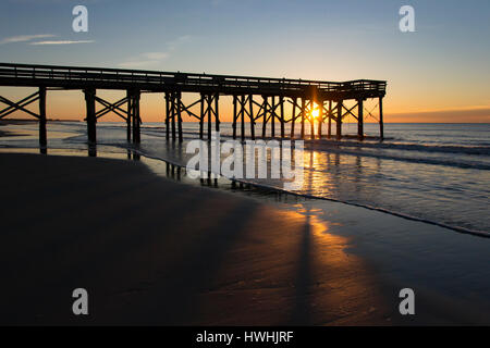 Sunrise con sole splendente di luce attraverso il molo in Silhouette Foto Stock