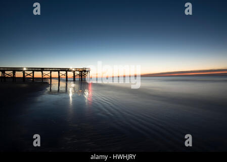 Vista Pre-Sunrise del molo con luci riflesse in oceano morbido Foto Stock