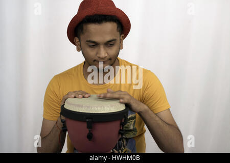 Un giovane uomo con Red Hat, t-shirt, suonando il djembe, perso in battiti Foto Stock