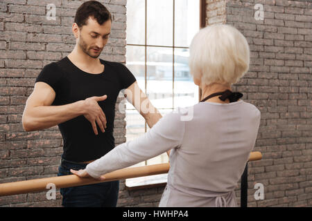 In fase di riscaldamento prima di ballare insieme. Atletica coinvolti artistico danza insegnamento del lettino di età della donna in piedi accanto alle barre e dimostrando righ Foto Stock