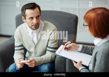 Premuto di mezza età paziente seduto nervosamente su comoda poltrona con fazzoletto in mani e spiegare i suoi problemi di coppia psicologo Foto Stock