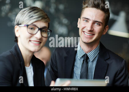 Piuttosto giovane imprenditrice in eleganti occhiali e la sua bella collega distratti dalla discussione del progetto e in posa per la fotografia con toothy Foto Stock