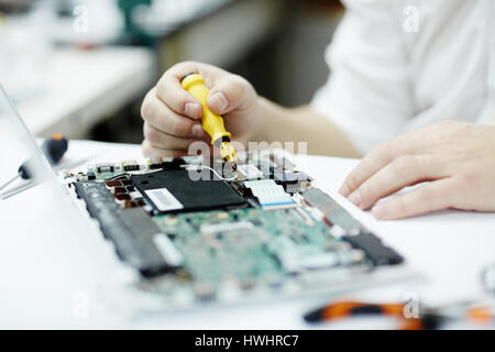 Closeup shot di un irriconoscibile uomo assemblaggio scheda di circuito in laptop usando un cacciavite e diversi strumenti sul tavolo in officina Foto Stock