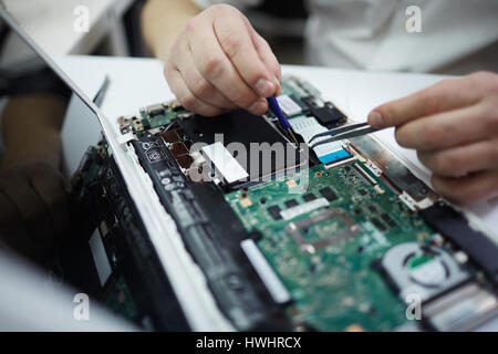 Closeup colpo di mani maschio riparazione di computer portatile usando un cacciavite e diversi strumenti sul tavolo in officina Foto Stock