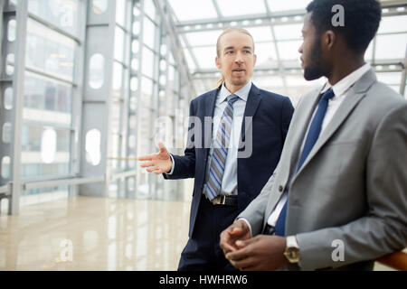 Ritratto di due imprenditori contemporanei, uno di loro africani, avente la conversazione in hall di vetro del moderno edificio per uffici Foto Stock