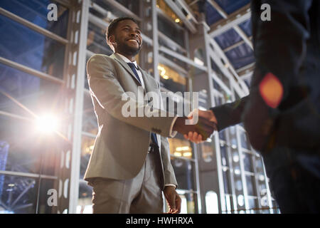 Angolo basso ritratto di due partner commerciali in stretta di mano: sorridente African -imprenditore americano stringono le mani con il collega caucasica nella hall della modalità Foto Stock