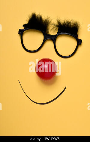 Un paio di occhiali con folte sopracciglia, un rosso clown naso e un sorriso disegnato su uno sfondo giallo Foto Stock