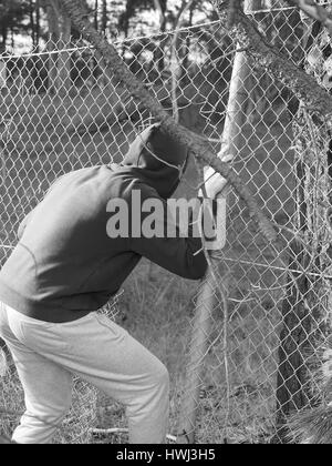 Persona strisciando attraverso una apertura di recinzione con mano aggrappati ad un filo di acciaio , in bianco e nero, Australia 2016 Foto Stock