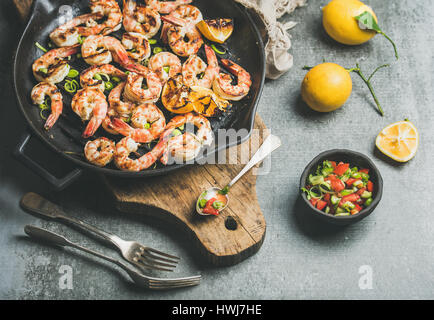 Cena a base di pesce. Grigliata di gamberi tigre in ghisa padella per grigliare con limone, porro, peperoncino e salsa alla menta salsa di cemento grigio Sfondo, sele Foto Stock