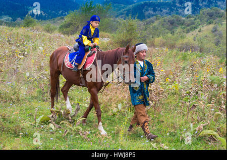 Il kazako uomo a camminare con il suo figlio su un cavallo dopo la circoncisione Sundet Toi cerimonia, il kazako villaggio etnografico Aul Gunny, Talgar città, Almaty in Kazakistan e in Asia Centrale, Asia, per il solo uso editoriale Foto Stock