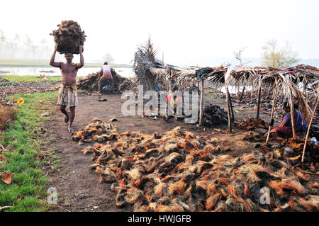 Un lavoratore assunzione di gusci di noce di cocco [lo strato esterno di pelle asportate] alla fabbrica di cocco. Foto Stock