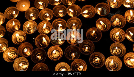 Molte candele accese con la calda fiamma durante il rito religioso Foto Stock