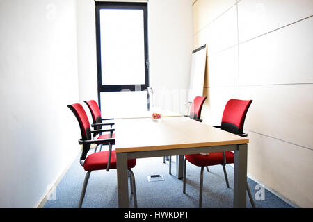 Luce di piccolo ufficio vuoto sala con tavolo e sedie rosse Foto Stock