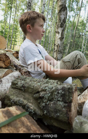 Ragazzo in appoggio sulla catasta di legna da ardere di log che ha aiutato a pila 10 anni d'età. Zawady Polonia centrale Europa Foto Stock