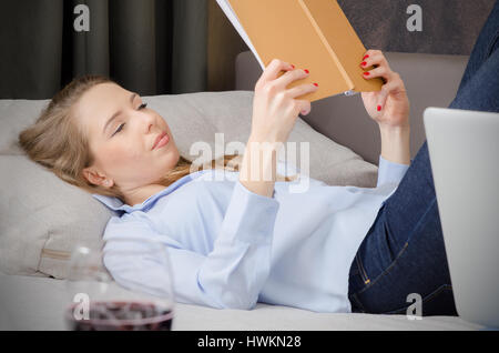 La donna posa sul divano e la lettura di un libro. prenota leggere donna recante divano rilassarsi leggendo godere di concetto Foto Stock