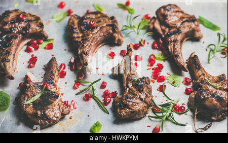 Grigliata di costolette di agnello con i semi di melograno, menta fresca e rosmarino su metallo vassoio di cottura sfondo, il fuoco selettivo composizione orizzontale. Bar a base di carne Foto Stock