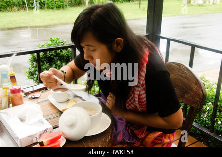 Donna tailandese di mangiare una zuppa di riso con carne di maiale in vaso di ceramica in mattina tempo al resort Foto Stock